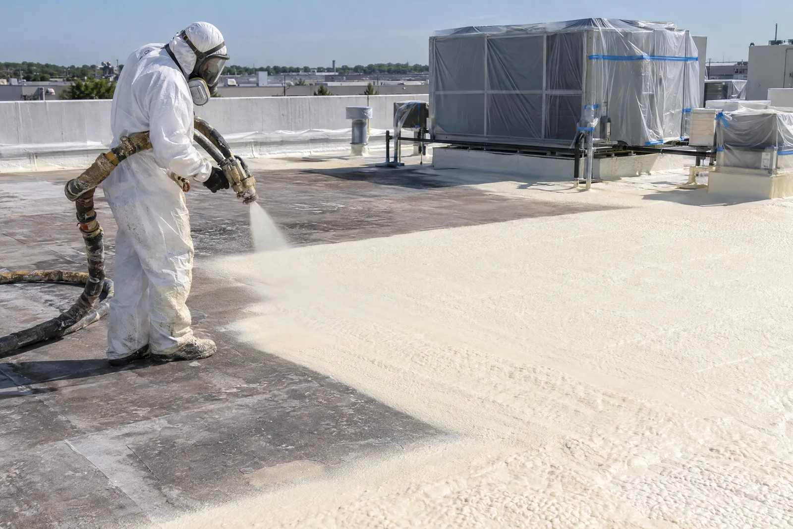 Worker applying spray foam roofing to a commercial roof